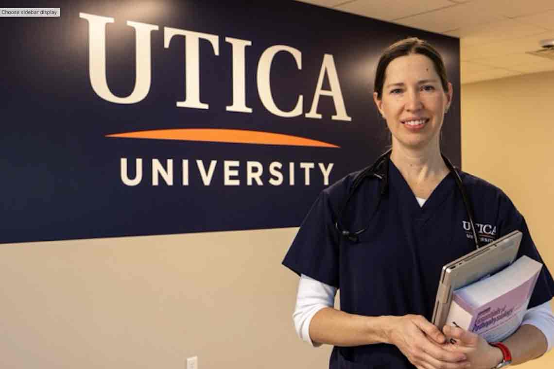 Utica nursing student standing in front of Utica's logo banner